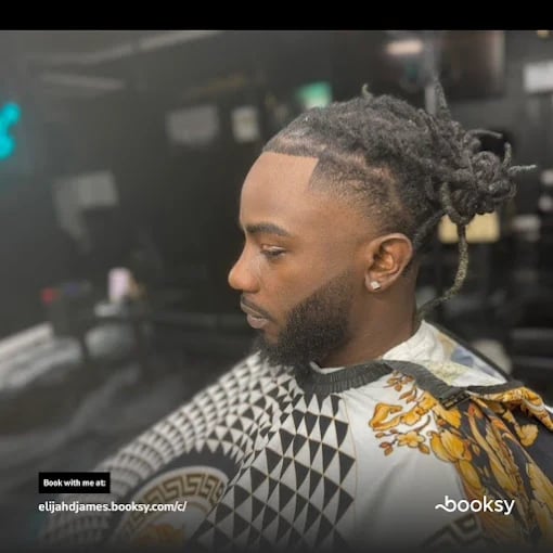 Man with dreadlocks and beard in geometric patterned jacket looking sideways