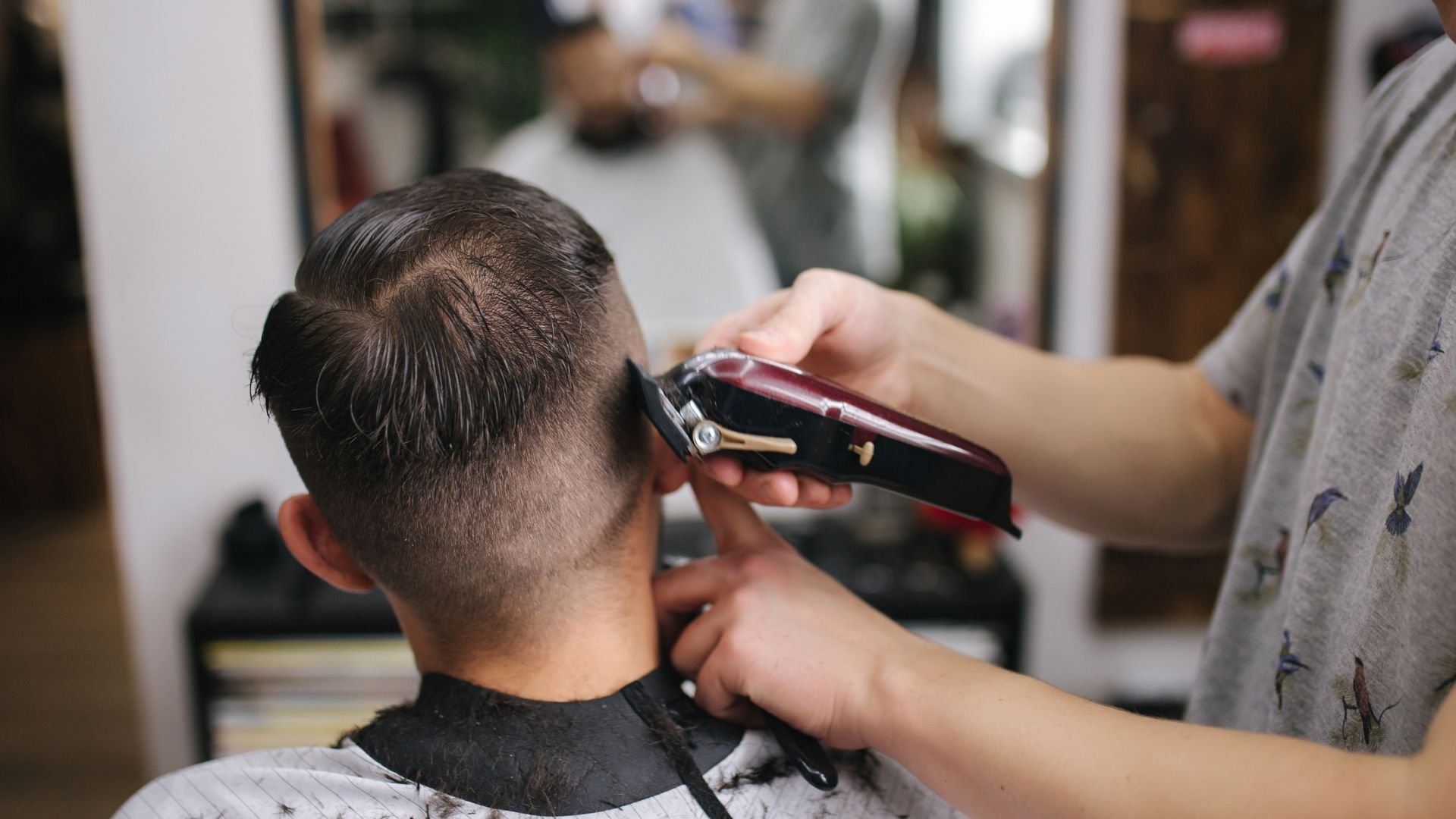 Barber using electric clipper to trim client's hair in barbershop