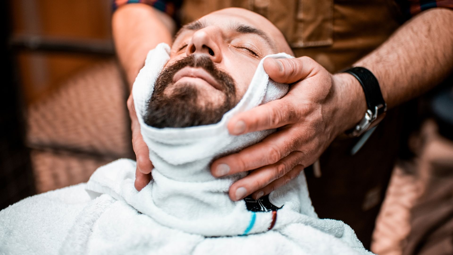 Bearded man relaxing during professional hot towel shave at barbershop