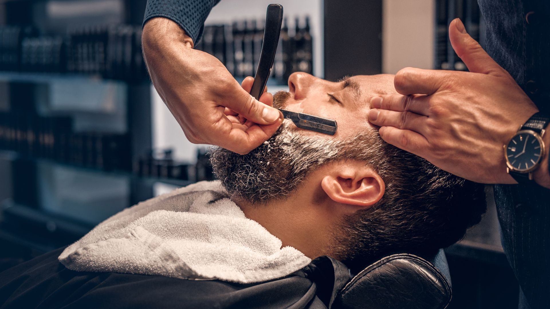Barber shaving client's beard with straight razor in barbershop