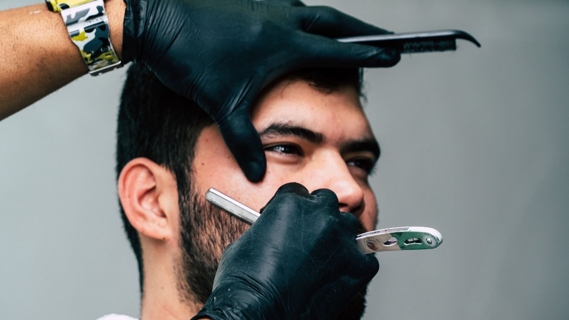 Barber in black gloves using straight razor for precise beard trimming